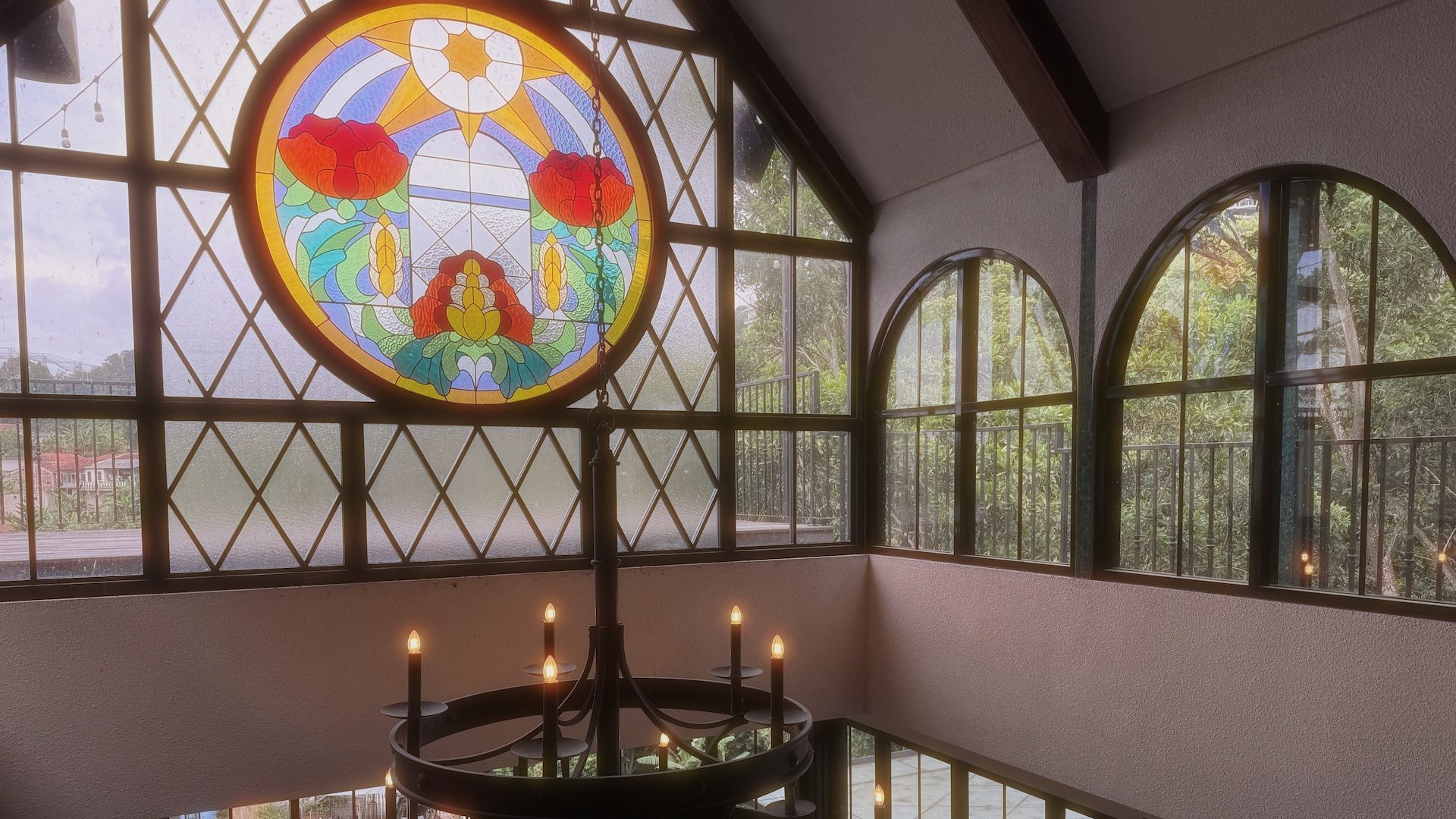 interior view of a room with large windows and a stained glass circular window featuring floral designs a chandelier with candles hangs from the ceiling digital production Interior view of a room with large windows and a stained glass circular window featuring floral designs. A chandelier with candles hangs from the ceiling.